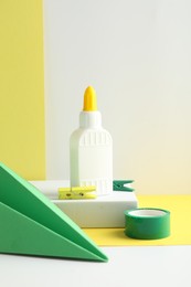 Photo of Glue in bottle, adhesive tape and green paper plane on color background, closeup