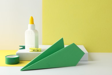 Photo of Glue in bottle, adhesive tape and green paper plane on color background, closeup