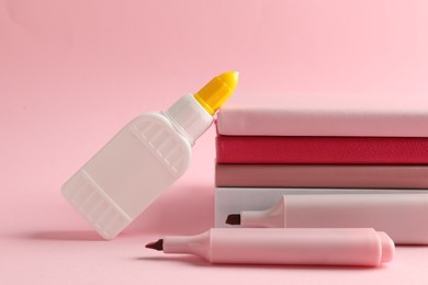 Photo of Glue in bottle, felt pens and notebooks on pink background, closeup