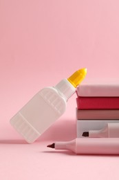 Photo of Glue in bottle, felt pens and notebooks on pink background, closeup
