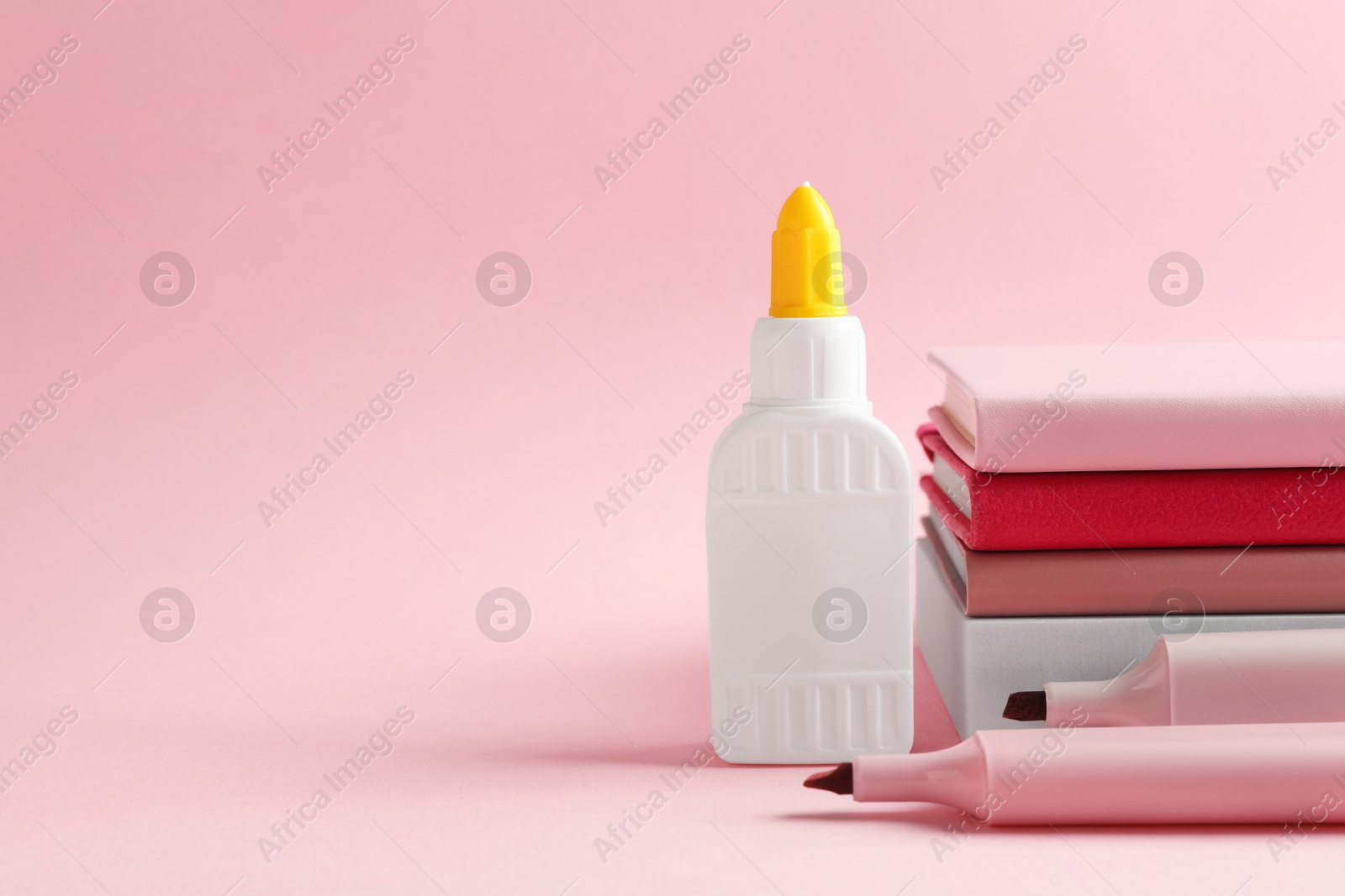 Photo of Glue in bottle, felt pens and notebooks on pink background, closeup. Space for text