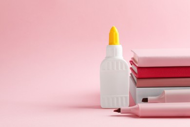 Photo of Glue in bottle, felt pens and notebooks on pink background, closeup. Space for text