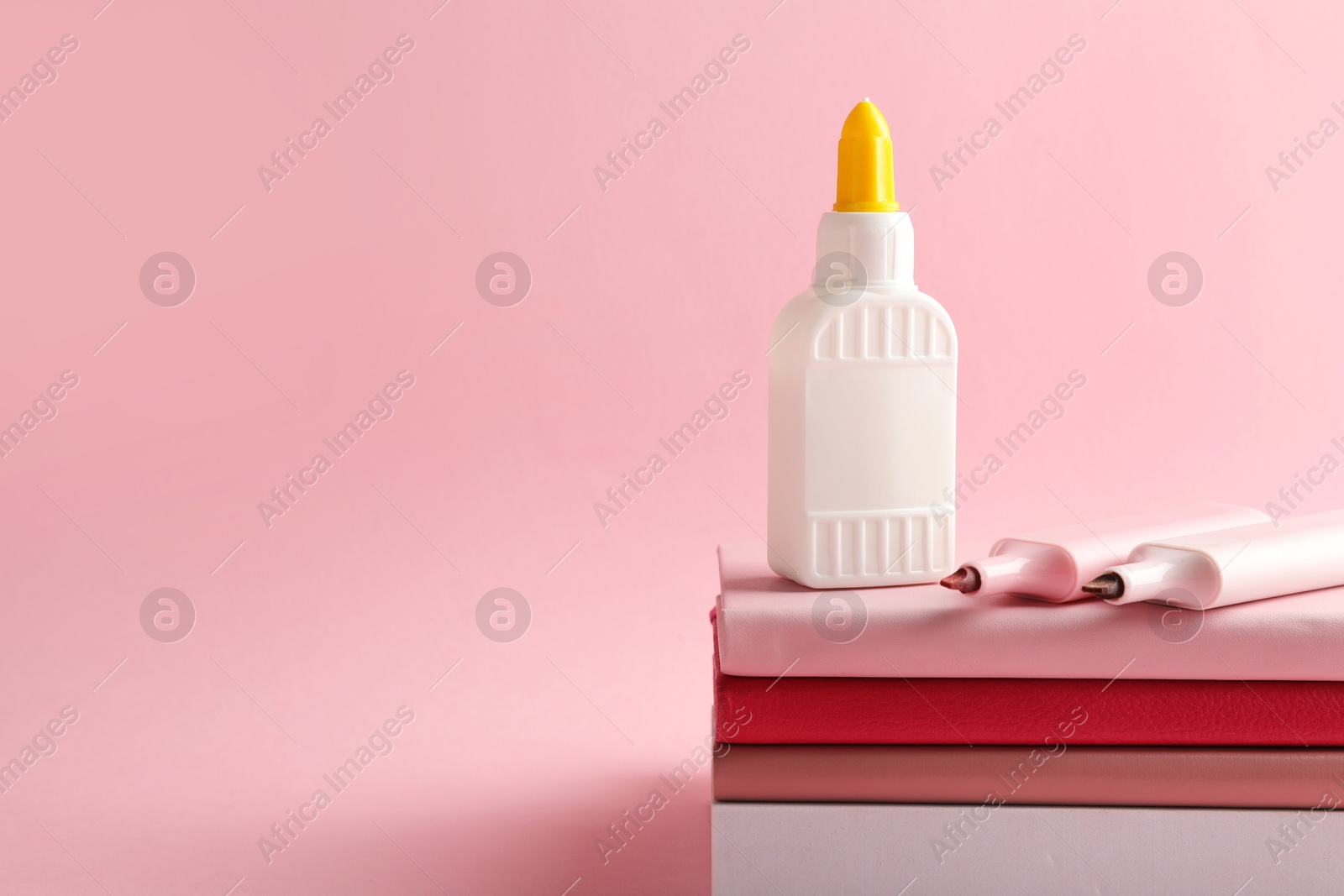 Photo of Glue in bottle, felt pens and notebooks on pink background, closeup. Space for text