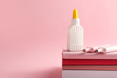 Photo of Glue in bottle, felt pens and notebooks on pink background, closeup. Space for text