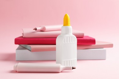 Photo of Glue in bottle, felt pens and notebooks on pink background, closeup