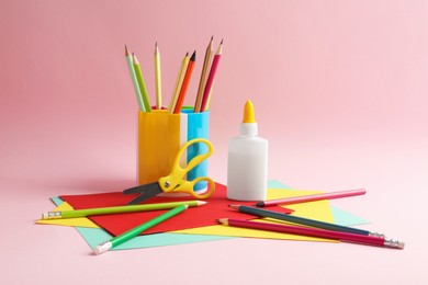 Photo of Glue in bottle, scissors, color pencils and paper on pink background, closeup