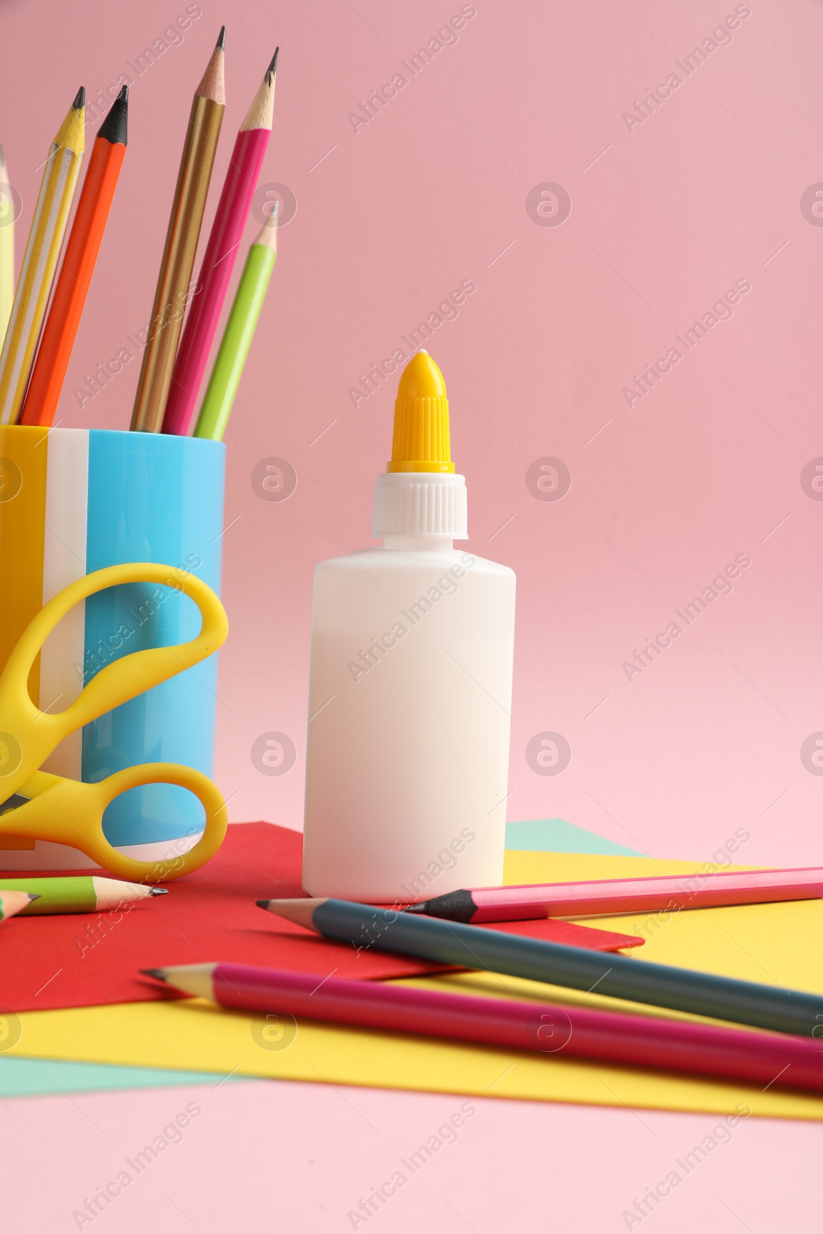 Photo of Glue in bottle, scissors, color pencils and paper on pink background, closeup