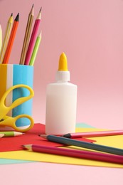 Photo of Glue in bottle, scissors, color pencils and paper on pink background, closeup