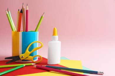 Photo of Glue in bottle, scissors, color pencils and paper on pink background, closeup. Space for text