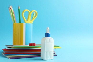 Photo of Glue in bottle and other stationery on light blue background, closeup. Space for text