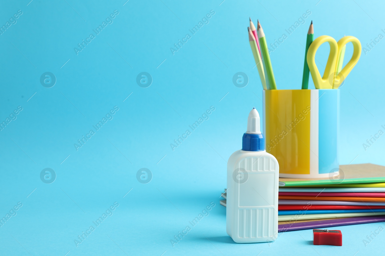 Photo of Glue in bottle and other stationery on light blue background, closeup. Space for text
