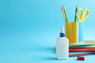 Photo of Glue in bottle and other stationery on light blue background, closeup. Space for text