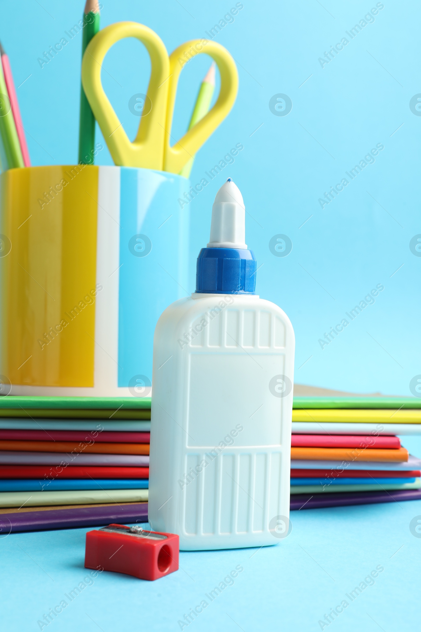Photo of Glue in bottle, sharpener, notebooks, color pencils and scissors on light blue background, closeup