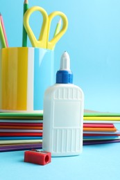 Photo of Glue in bottle, sharpener, notebooks, color pencils and scissors on light blue background, closeup