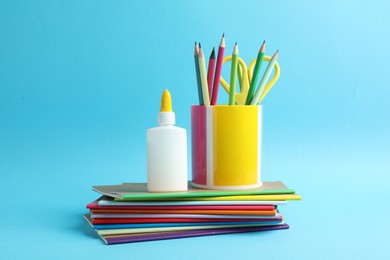 Photo of Glue in bottle, notebooks, color pencils and scissors on light blue background, closeup