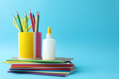 Photo of Glue in bottle, notebooks, color pencils and scissors on light blue background, closeup. Space for text