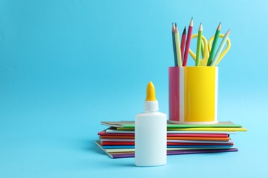 Photo of Glue in bottle, notebooks, color pencils and scissors on light blue background, closeup. Space for text