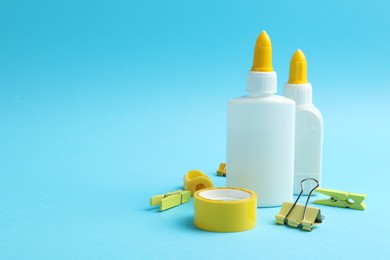Photo of Glue in bottles, binder clip, sharpener and adhesive tape on light blue background, closeup. Space for text