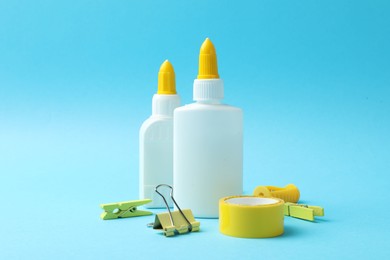 Photo of Glue in bottles, binder clip, sharpener and adhesive tape on light blue background, closeup