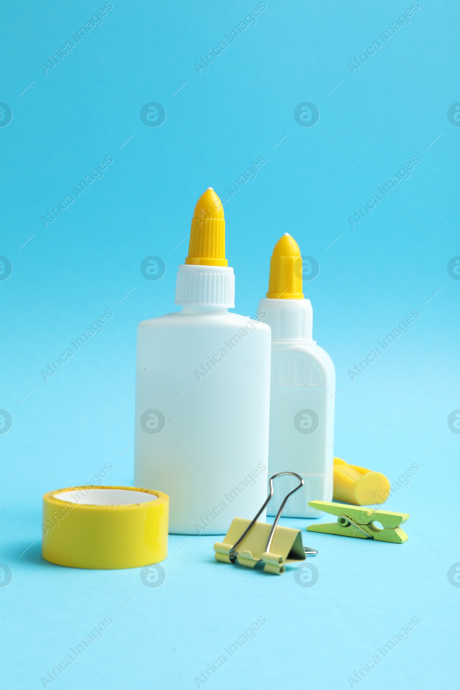 Photo of Glue in bottles, binder clip, sharpener and adhesive tape on light blue background