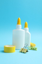 Photo of Glue in bottles, binder clip, sharpener and adhesive tape on light blue background