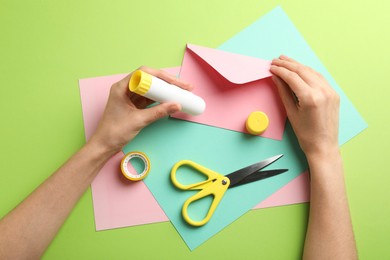 Photo of Woman making craft with glue and color paper at green table, top view