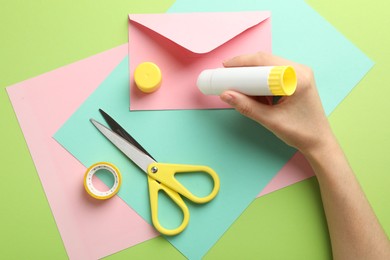 Photo of Woman making craft with glue and color paper at green table, top view