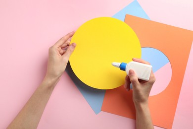 Photo of Woman making craft with glue and color paper at pink table, top view