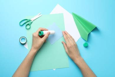 Photo of Woman making craft with glue and color paper at light blue table, top view