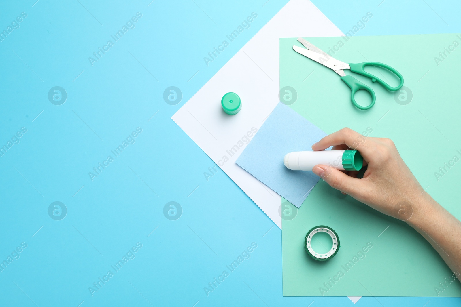 Photo of Woman making craft with glue and color paper at light blue table, top view. Space for text