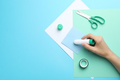 Photo of Woman making craft with glue and color paper at light blue table, top view. Space for text