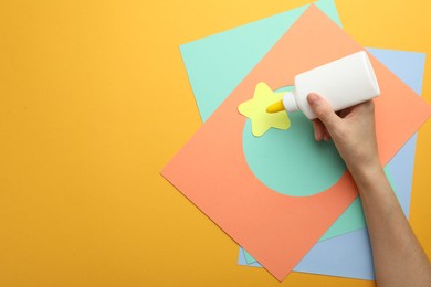 Photo of Woman making craft with glue and color paper at orange table, top view. Space for text
