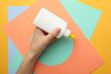 Photo of Woman making craft with glue and color paper at orange table, top view