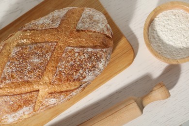 Photo of Loaf of fresh bread, flour and rolling pin on white wooden table, flat lay