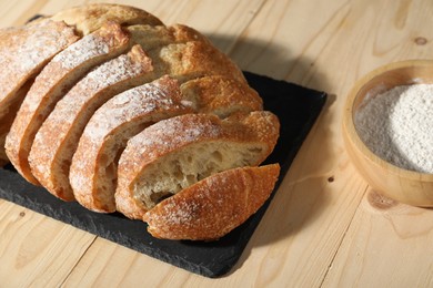 Photo of Fresh cut bread and flour on light wooden table, closeup