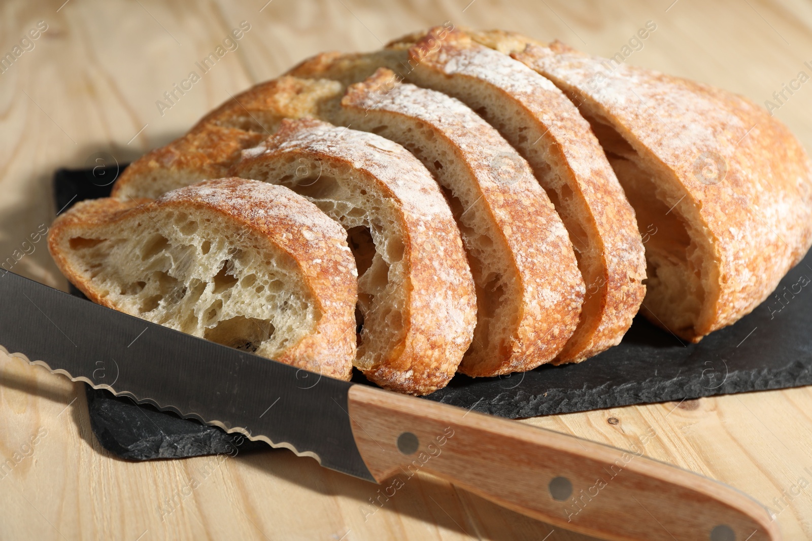 Photo of Fresh cut bread and knife on light wooden table, closeup