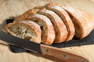 Photo of Fresh cut bread and knife on light wooden table, closeup