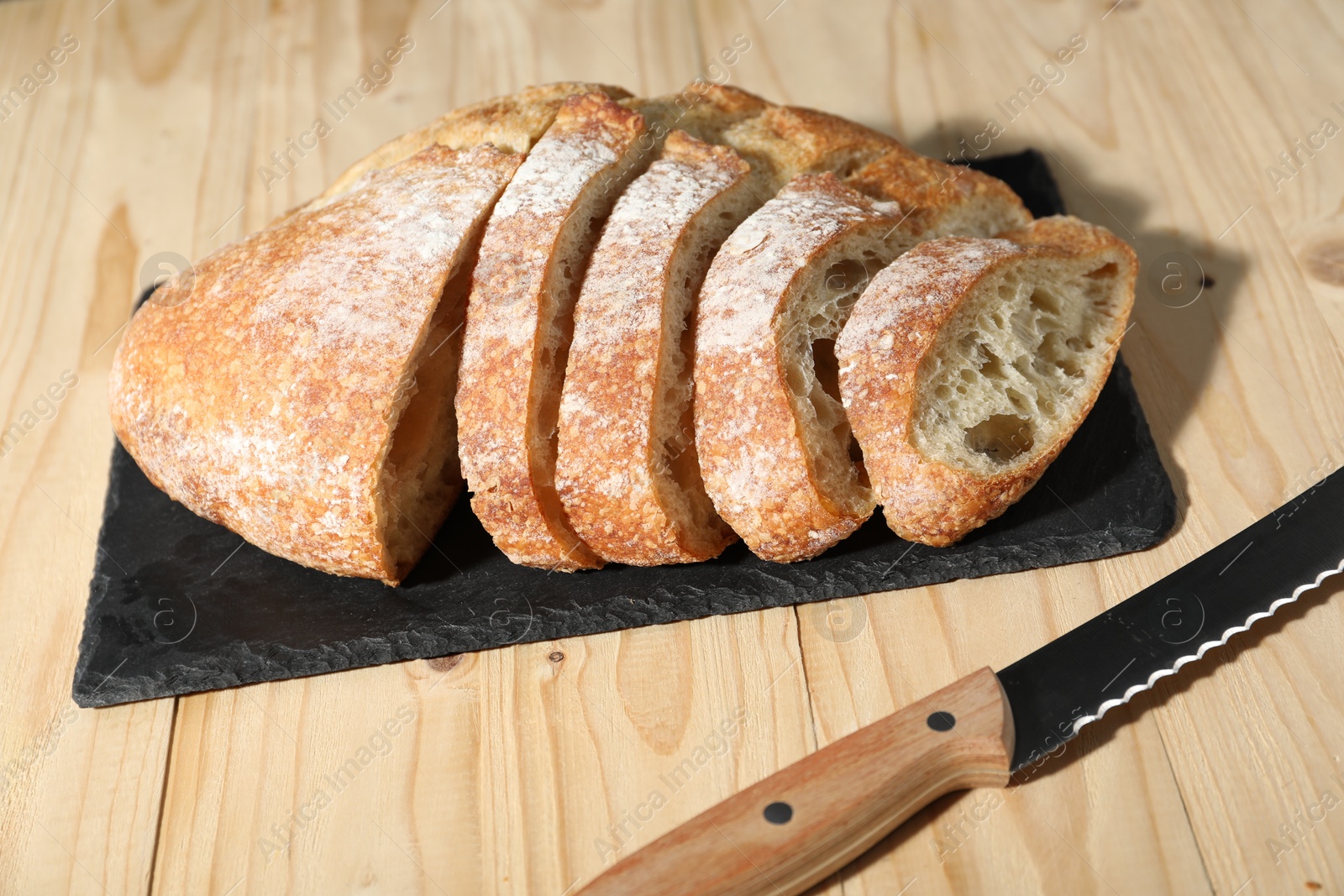 Photo of Fresh cut bread and knife on light wooden table, closeup