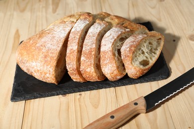 Photo of Fresh cut bread and knife on light wooden table, closeup