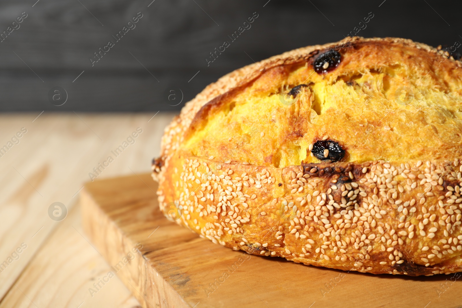 Photo of Loaf of fresh bread with sesame seeds and raisins on light wooden table, closeup. Space for text