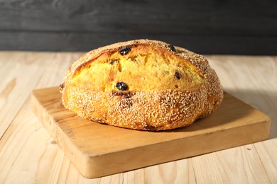 Photo of Loaf of fresh bread with sesame seeds and raisins on light wooden table, closeup