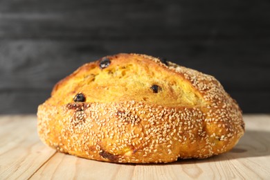 Photo of Loaf of fresh bread with sesame seeds and raisins on light wooden table, closeup