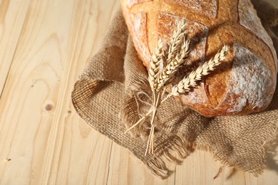 Photo of Loaf of fresh bread and spikelets on light wooden table, closeup. Space for text