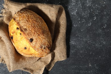 Photo of Loaf of fresh bread with sesame seeds and raisins on grey textured table, top view. Space for text