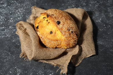 Photo of Loaf of fresh bread with sesame seeds and raisins on grey textured table
