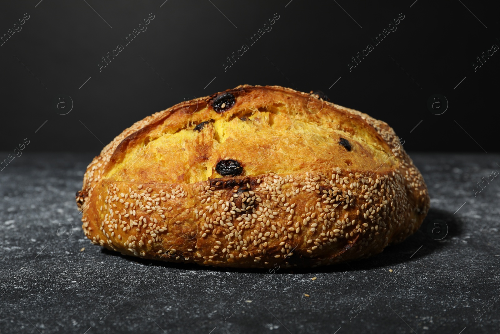 Loaf of fresh bread with sesame seeds and raisins on grey textured table, closeup Photo of Loaf of fresh bread with sesame seeds and raisins on grey textured table, closeup
