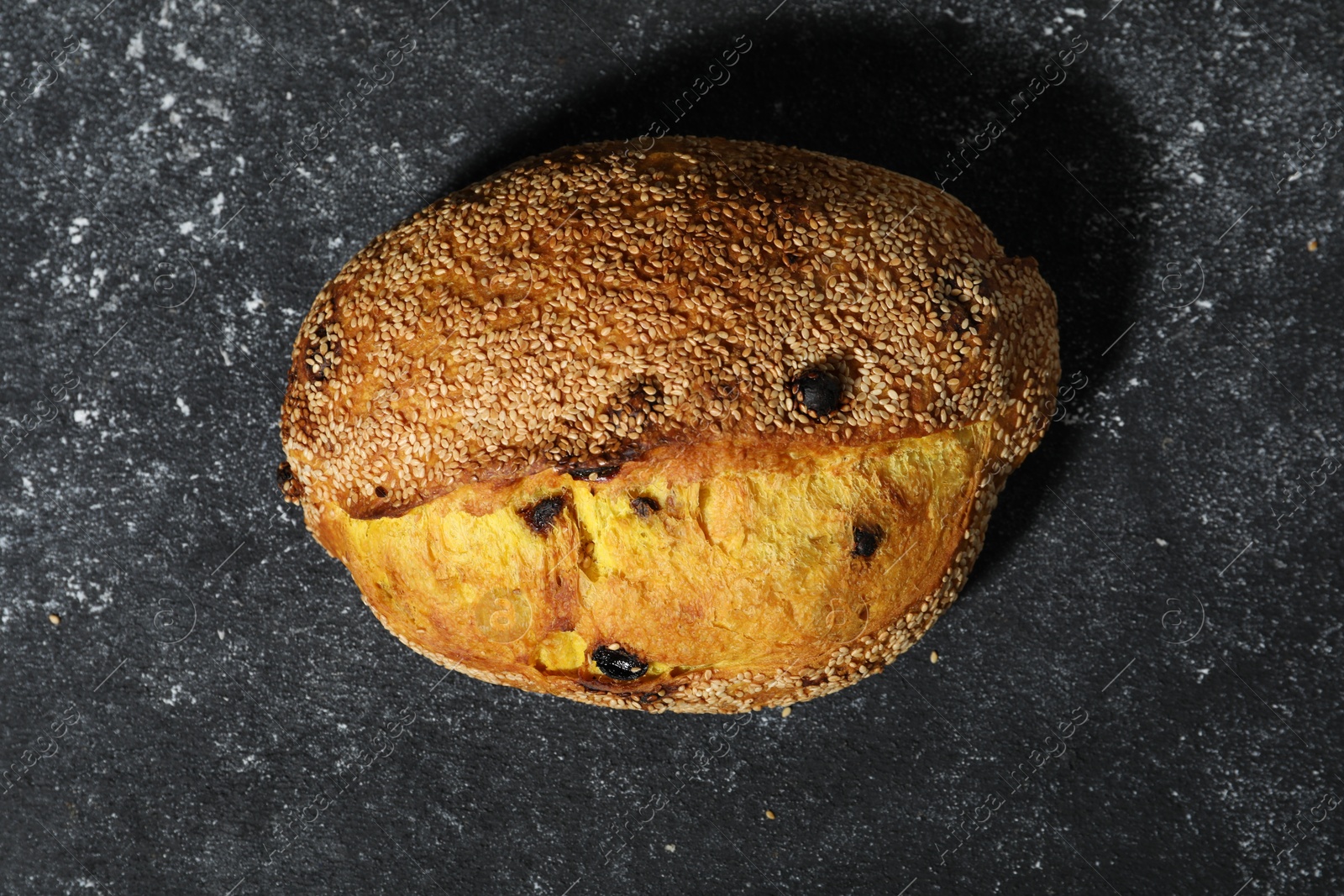 Loaf of fresh bread with sesame seeds and raisins on grey textured table, top view Photo of Loaf of fresh bread with sesame seeds and raisins on grey textured table, top view
