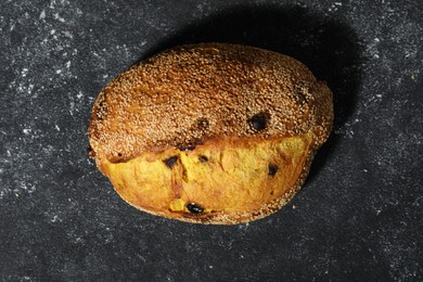 Photo of Loaf of fresh bread with sesame seeds and raisins on grey textured table, top view