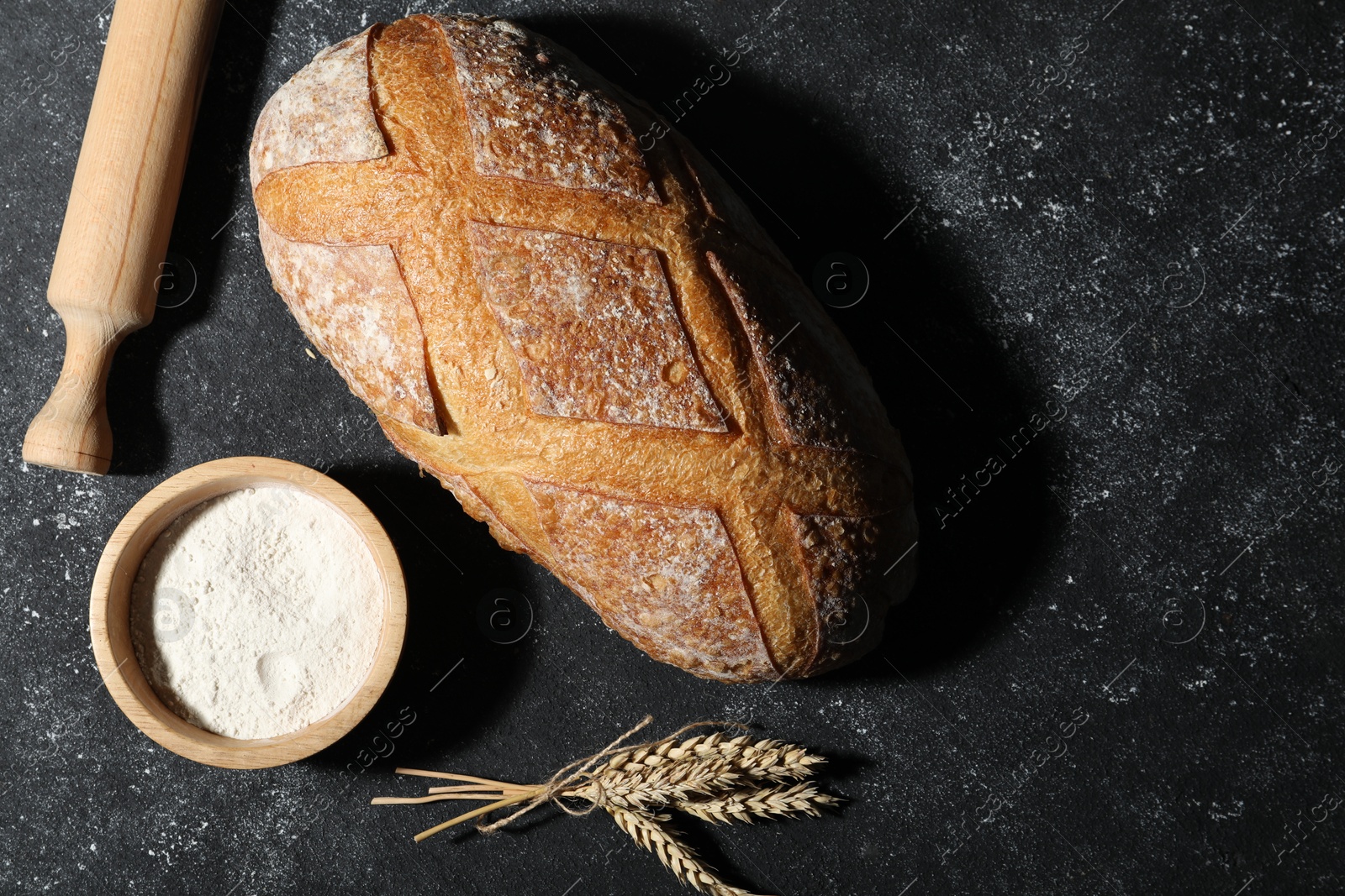 Loaf of fresh bread, rolling pin, flour and spikelets on grey textured table, flat lay. Space for text Photo of Loaf of fresh bread, rolling pin, flour and spikelets on grey textured table, flat lay. Space for text
