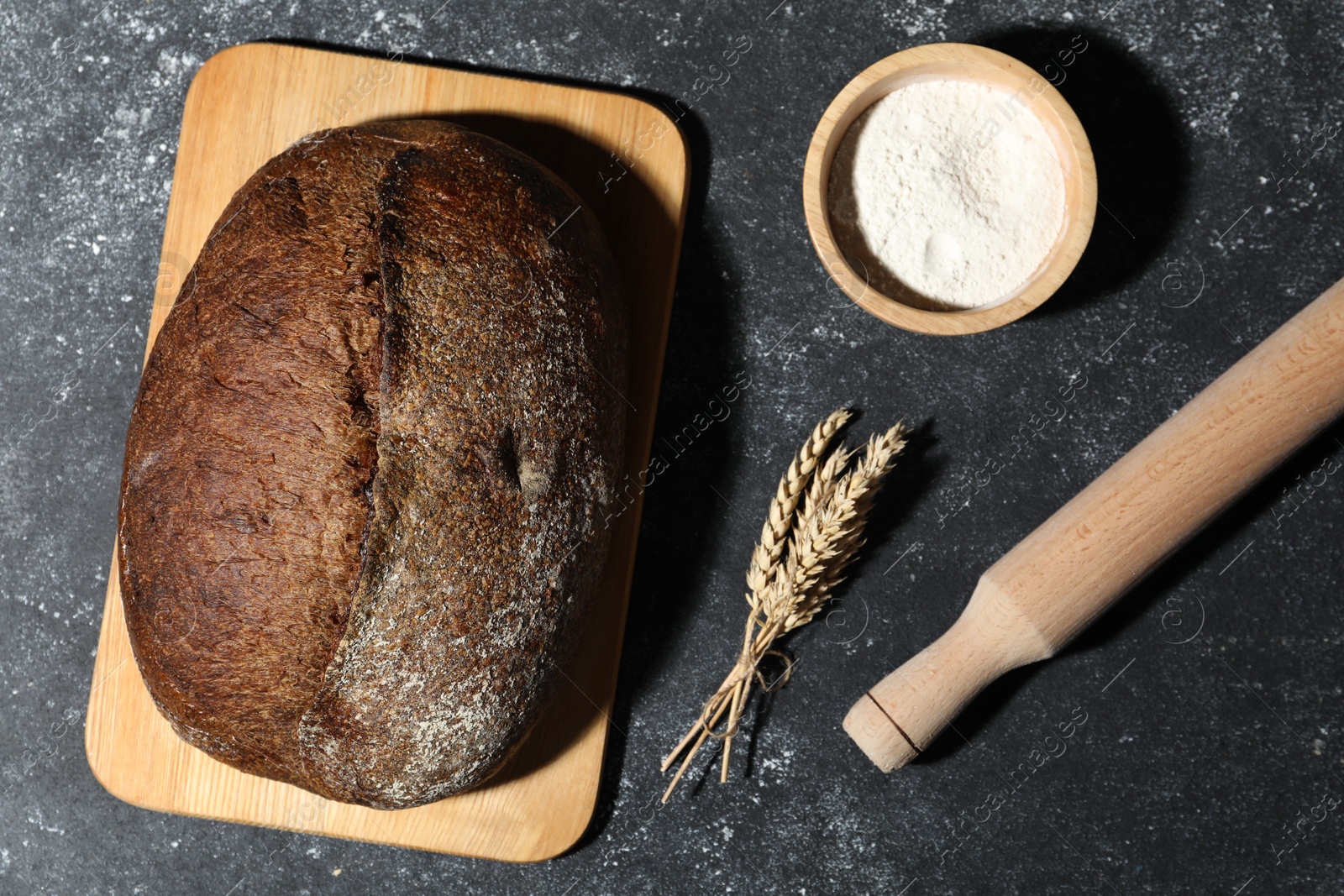Loaf of fresh bread, flour and rolling pin on grey textured table, flat lay Photo of Loaf of fresh bread, flour and rolling pin on grey textured table, flat lay